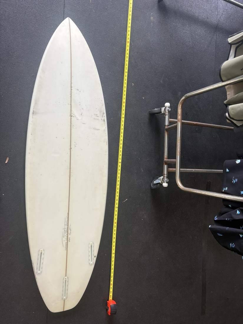 Stamps 5'10 surfboard bottom, nose up, measuring tape on right